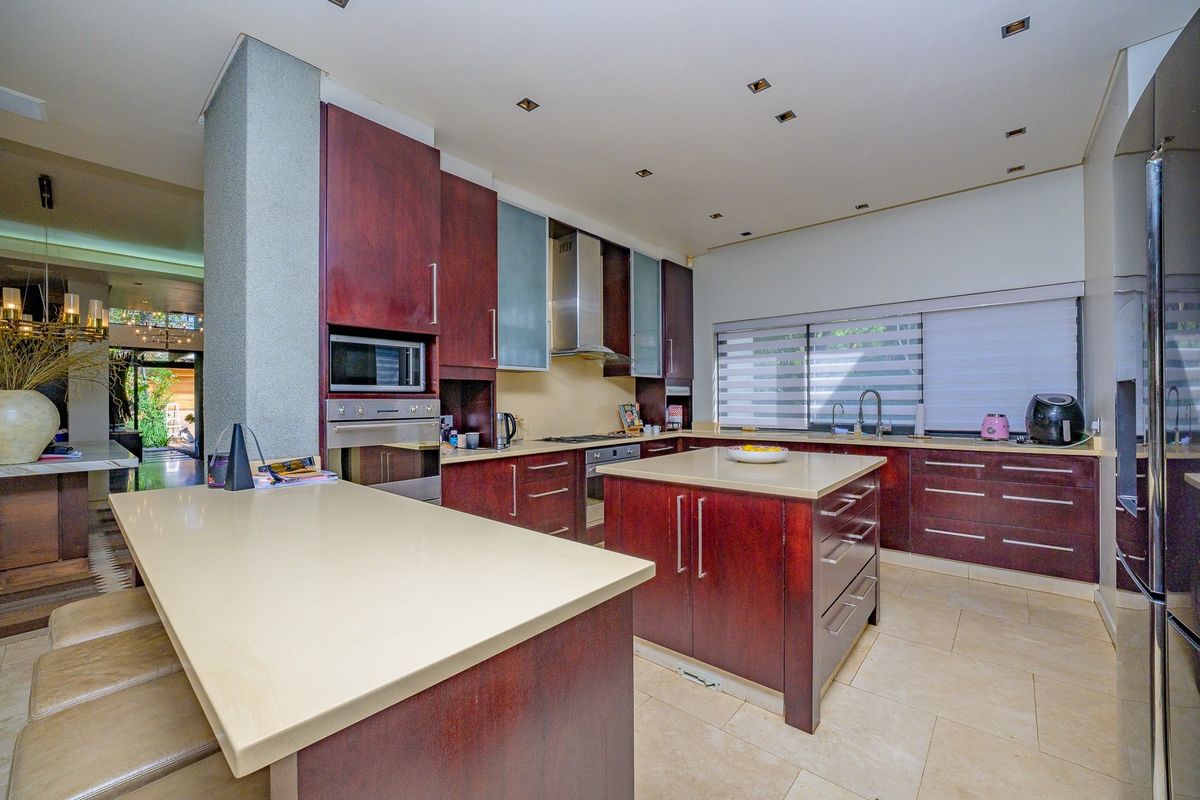 Modern kitchen featuring dark wood cabinetry, stone countertops, a central island, and integrated appliances with recessed lighting and tiled flooring.