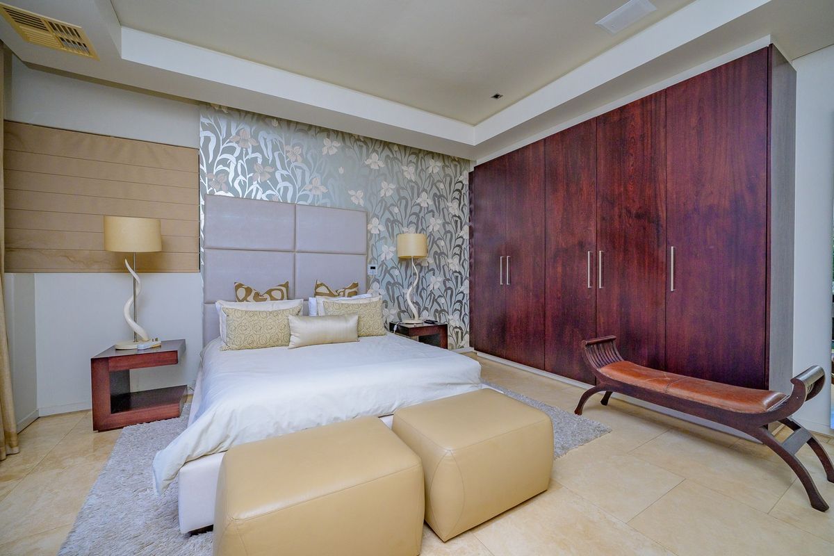 Spacious bedroom featuring extensive dark wood built-in cupboards, a decorative feature wall, recessed ceiling lighting, and neutral tiled flooring.