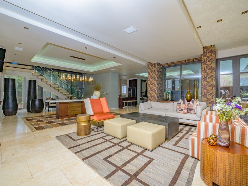 Spacious open-plan living area featuring stone flooring, a modern floating staircase with glass balustrade, and recessed ceiling lighting with integrated kitchen access.