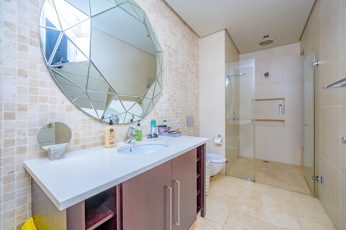Modern bathroom featuring a vanity with integrated sink, mosaic tiled wall, and a spacious walk-in shower with a glass screen and recessed niche.