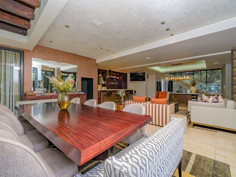 Spacious open-plan living and dining area featuring stone flooring, recessed lighting, a built-in bar, and a modern staircase with a glass balustrade.
