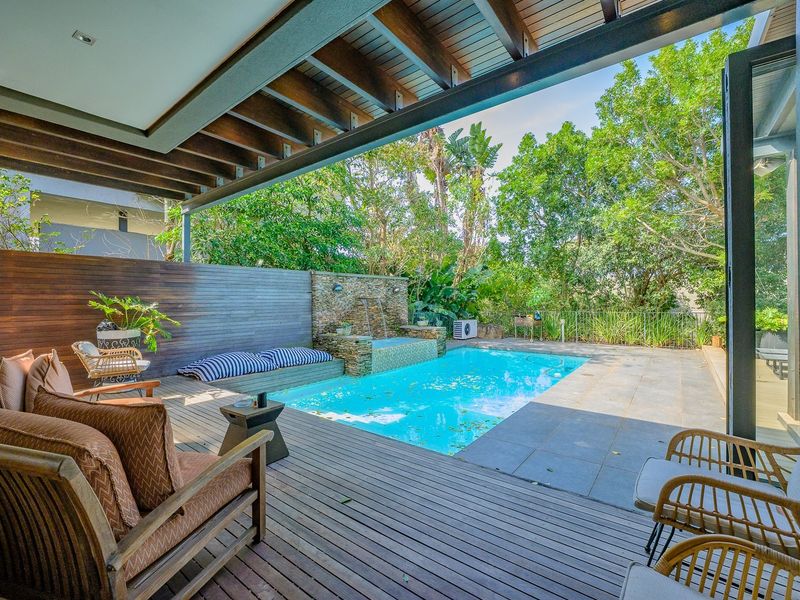 Outdoor entertainment area featuring a swimming pool, stone water feature, and timber decking under a covered patio with exposed beams.