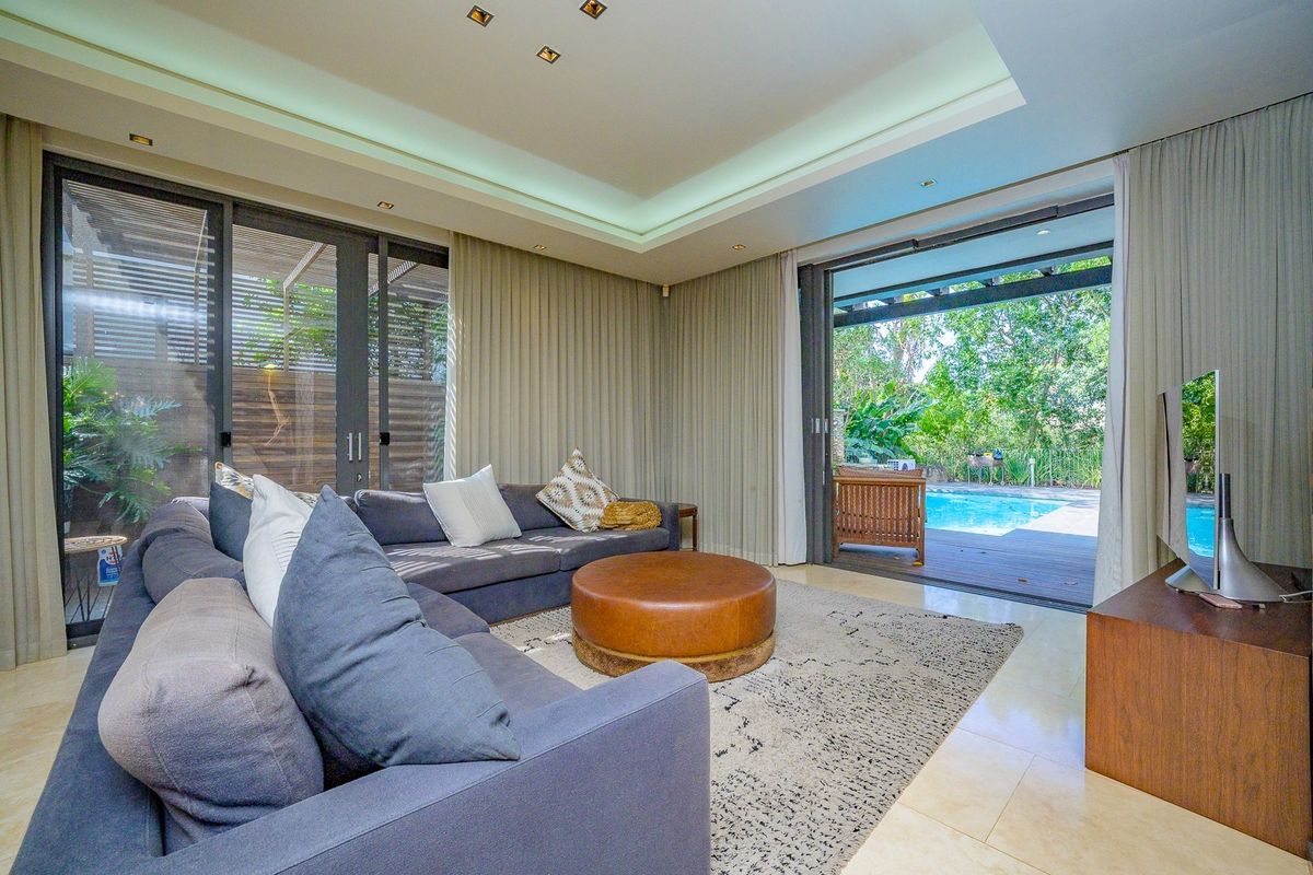 Modern living room featuring recessed ceiling lighting, cove lighting, and large sliding glass doors that open onto a patio and swimming pool area.