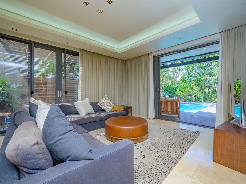 Modern living room featuring recessed ceiling lighting, cove lighting, and large sliding glass doors that open onto a patio and swimming pool area.
