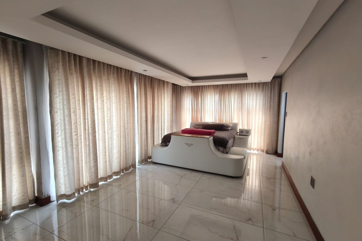 Spacious bedroom featuring polished tiled flooring, a recessed ceiling design, and floor-to-ceiling curtains providing ample natural light.