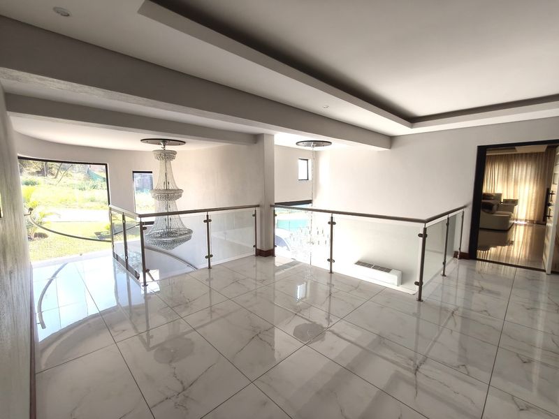 Spacious upper-level landing featuring polished porcelain floor tiles, a modern glass balustrade, and elegant recessed ceiling details overlooking the staircase void.
