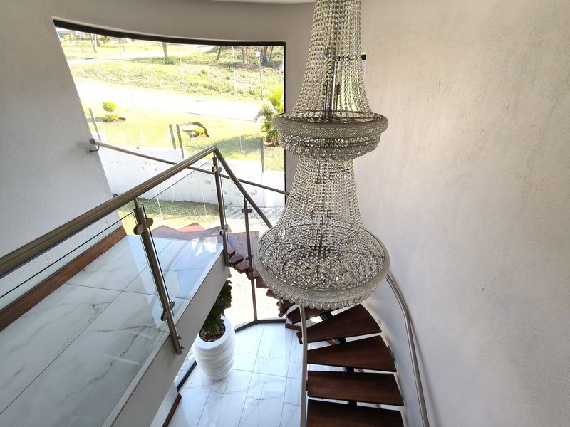 Elegant entrance hallway featuring a striking spiral staircase with glass balustrades, marble-look flooring, and a prominent crystal chandelier.