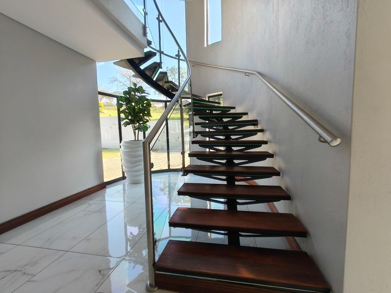 Modern entrance hallway featuring a striking floating staircase with timber treads, glass balustrades, and large floor-to-ceiling windows providing ample natural light.