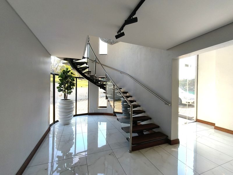Modern entrance hall featuring a striking spiral staircase with glass balustrades, polished porcelain tile flooring, and abundant natural light from floor-to-ceiling windows.