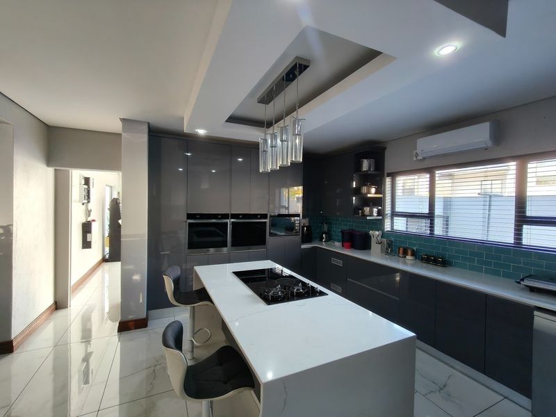 Modern kitchen featuring high-gloss cabinetry, a central island with integrated hob, stone countertops, subway tile backsplash, and recessed ceiling lighting.