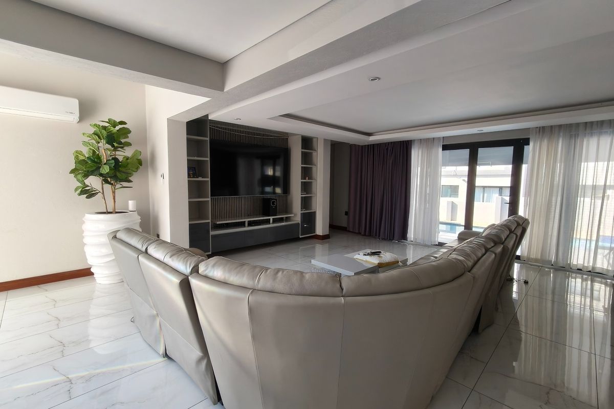 Spacious living room featuring polished marble-look tiled floors, a custom built-in media wall, recessed ceiling lighting, and large sliding doors leading to the pool area.