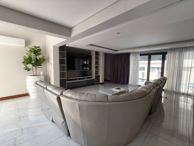 Spacious living room featuring polished marble-look tiled floors, a custom built-in media wall, recessed ceiling lighting, and large sliding doors leading to the pool area.