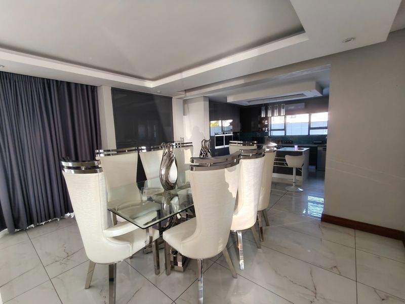 Modern open-plan dining and kitchen area featuring marble-look floor tiles, recessed ceiling lighting, and a sleek kitchen with built-in appliances.