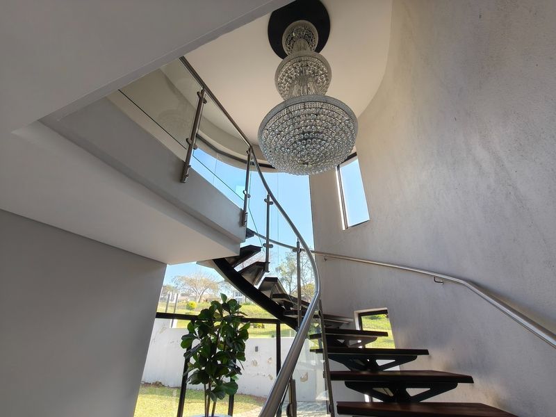 Elegant spiral staircase featuring timber treads, a glass balustrade with stainless steel handrail, and a prominent crystal chandelier in a bright, modern hallway.