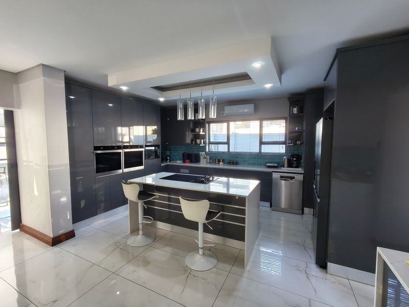 Modern kitchen featuring high-gloss cabinetry, a central island with integrated cooktop, double built-in ovens, and elegant marble-look floor tiles.