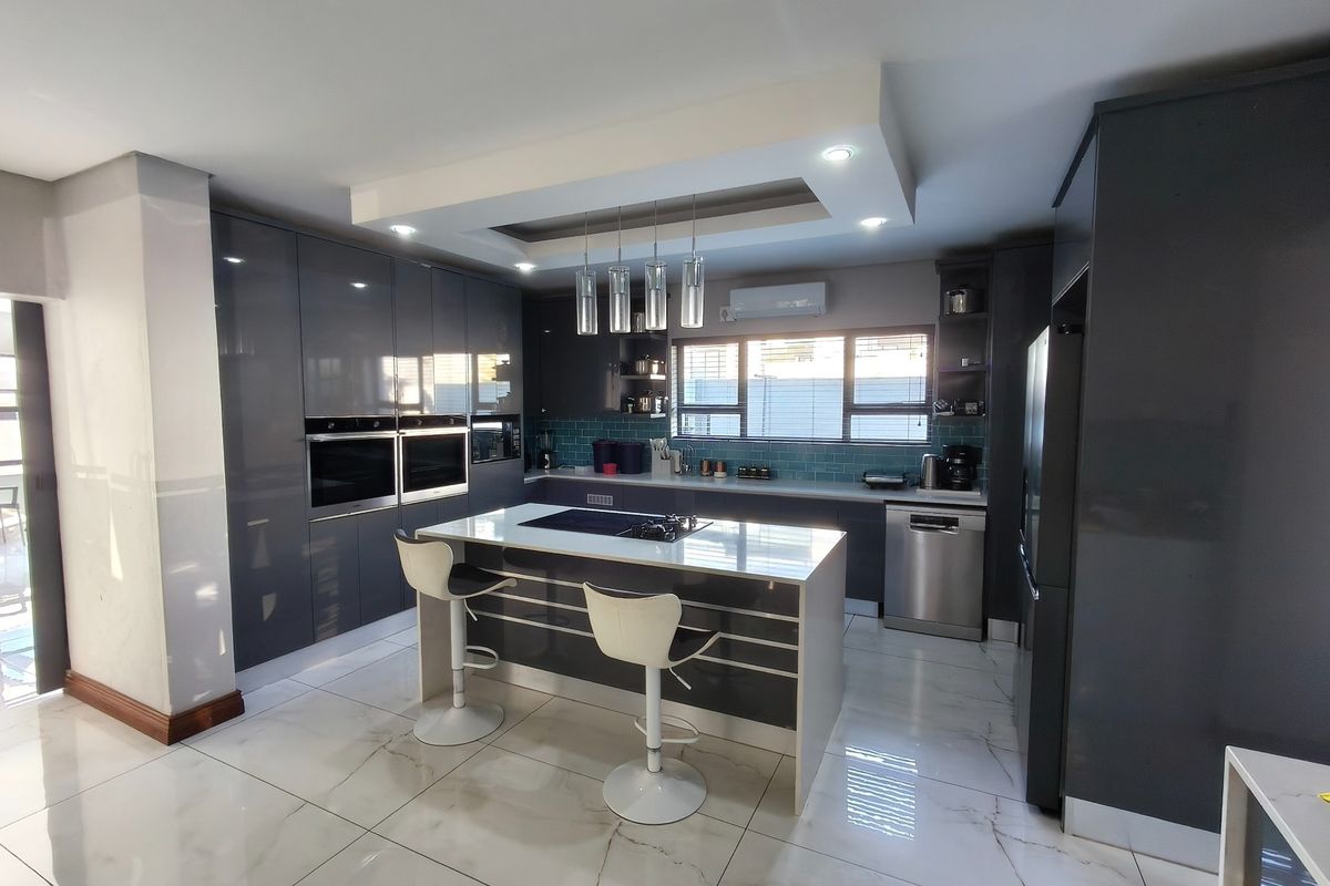 Modern kitchen featuring high-gloss cabinetry, a central island with integrated cooktop, double built-in ovens, and elegant marble-look floor tiles.