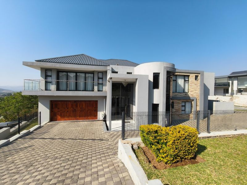 Modern double-story residential property featuring a paved driveway, double garage, stone-clad accents, and an upper-level balcony with glass balustrades.