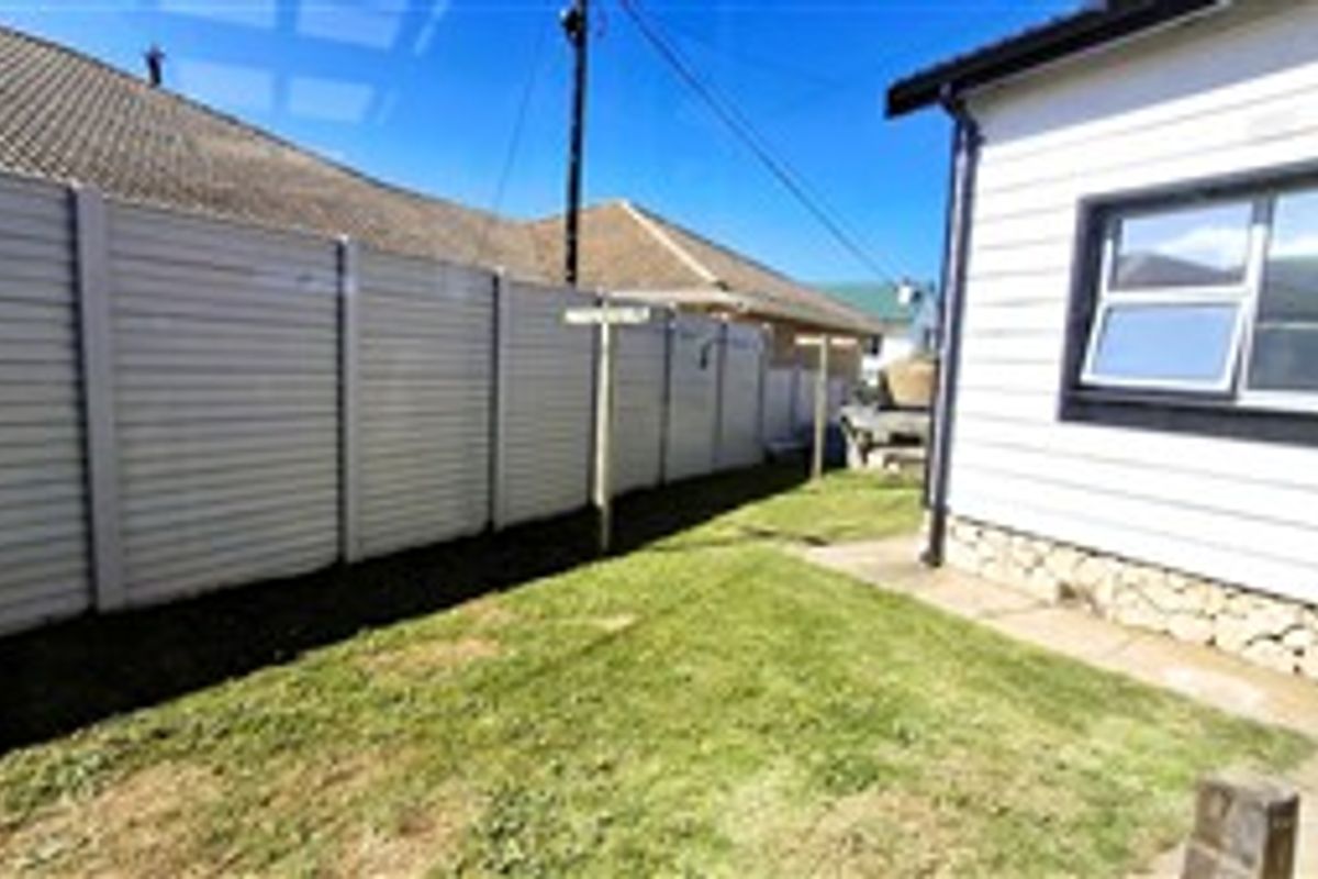 A view of the rear exterior of the house featuring vinyl siding, stone foundation detailing, and a private lawn area enclosed by a boundary wall.