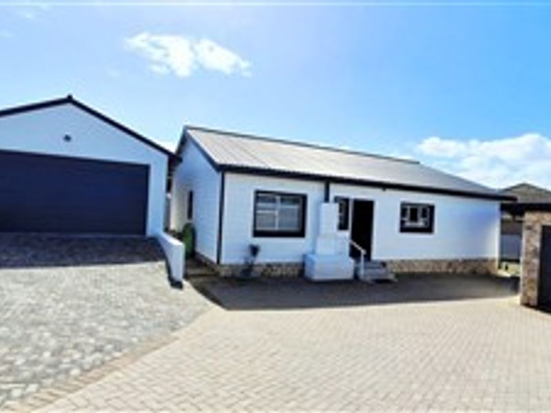 Front view of the property featuring a white facade, metal roofing, stone cladding accents, and multiple garage spaces with a paved driveway.