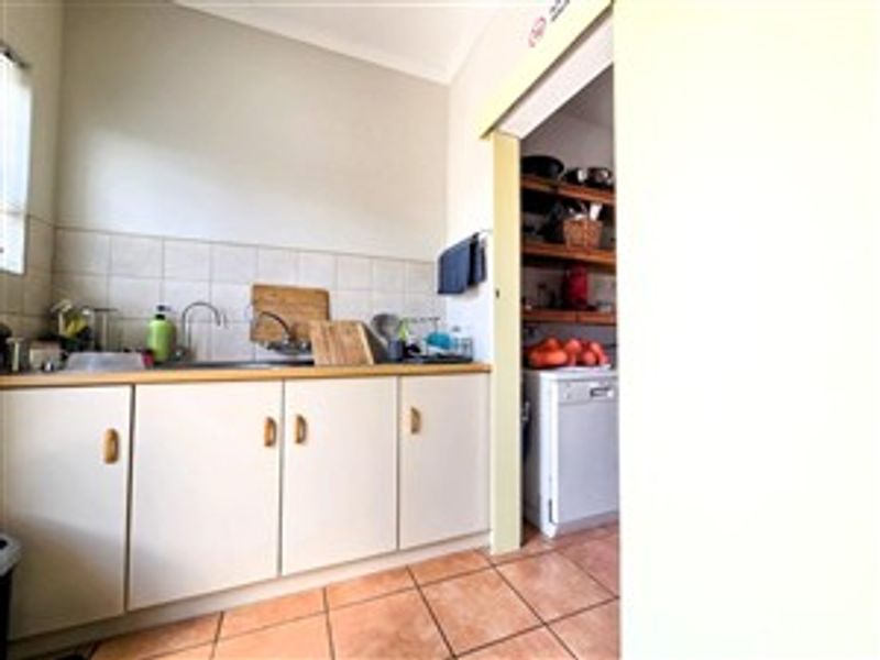 A functional scullery area featuring built-in cabinetry, a stainless steel sink, tiled splashback, and durable tiled flooring, providing additional prep and wash-up space.