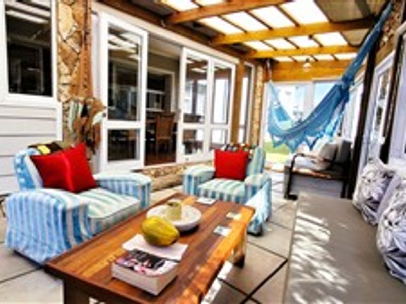 A covered outdoor patio area featuring a timber pergola, stone wall accents, and large sliding glass doors providing access to the interior living space.
