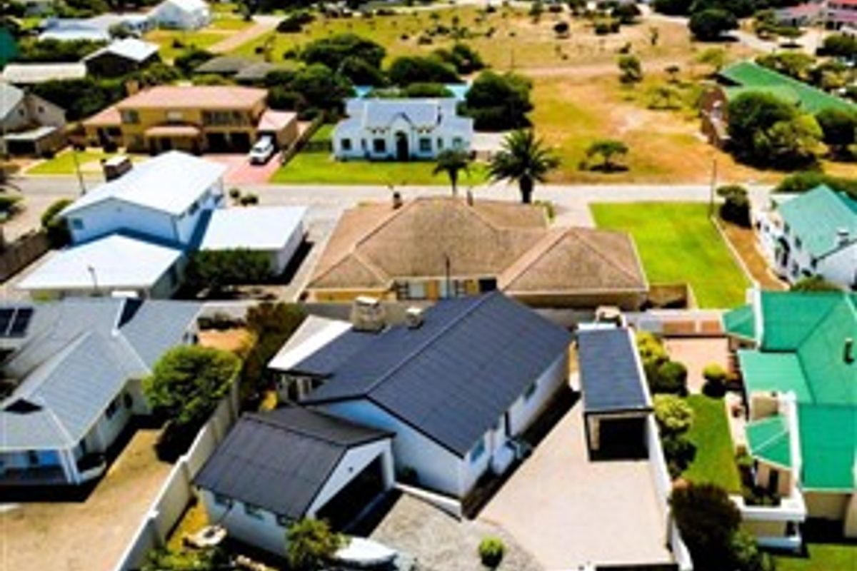 Aerial view of the property showcasing the roof structure, paved driveway, carport, and surrounding coastal residential neighborhood.