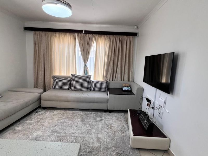 A comfortable living room featuring tiled flooring, neutral wall finishes, and large window treatments, providing a functional and well-lit space for relaxation.