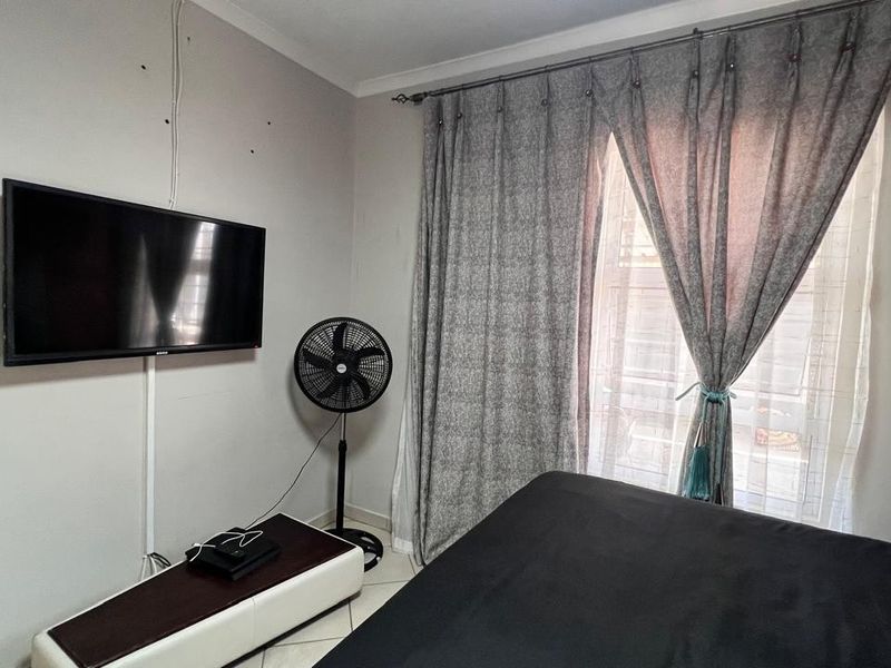 A bedroom featuring tiled flooring and a window with curtain tracks, currently showing signs of wall damage and exposed wiring.