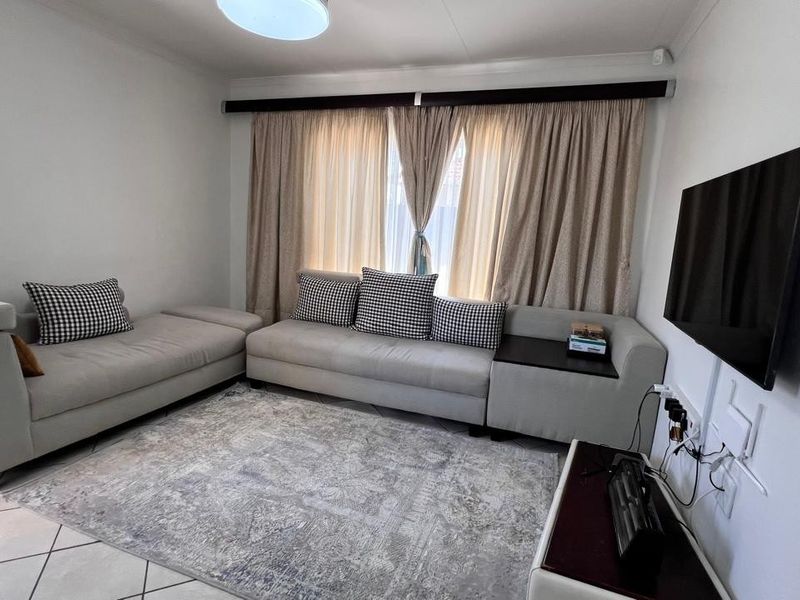 A comfortable living room featuring tiled flooring, neutral wall finishes, and a wall-mounted television setup with integrated curtain tracks.