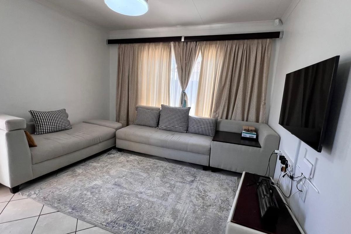 A comfortable living room featuring tiled flooring, neutral wall finishes, and a wall-mounted television setup with integrated curtain tracks.