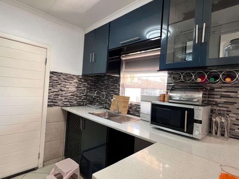 A compact kitchen featuring modern dark blue cabinetry, stone countertops, and a decorative mosaic tile backsplash with integrated sink and storage.
