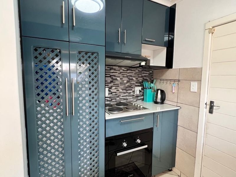 Compact kitchen featuring modern blue high-gloss cabinetry, built-in oven, electric hob, extractor fan, and a decorative tiled backsplash.