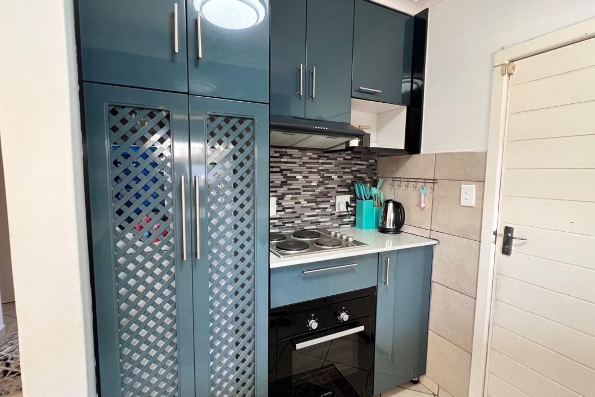 Compact kitchen featuring modern blue high-gloss cabinetry, built-in oven, electric hob, extractor fan, and a decorative tiled backsplash.