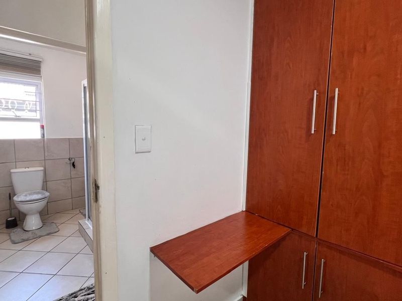 A hallway area featuring built-in wooden cabinetry and a wall-mounted desk, with a view into an adjacent tiled bathroom.