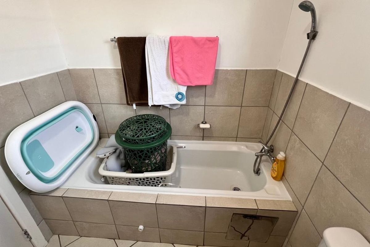A functional bathroom featuring a built-in bathtub with tiled surround and a shower mixer, showing minor wear on the tile finish.