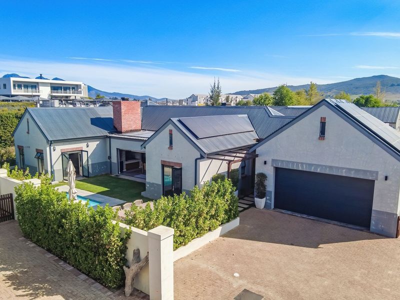 Aerial view of a modern residential property featuring a metal roof with solar panels, a swimming pool, and a spacious paved driveway.