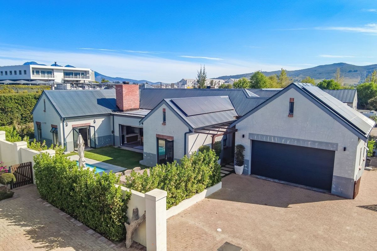 Aerial view of a modern residential property featuring a metal roof with solar panels, a swimming pool, and a spacious paved driveway.