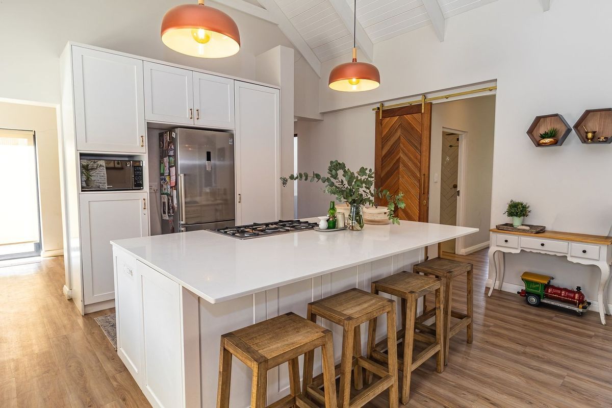 Modern kitchen featuring a central island with gas cooktop, white cabinetry, vaulted ceilings, and a stylish wooden sliding barn door.