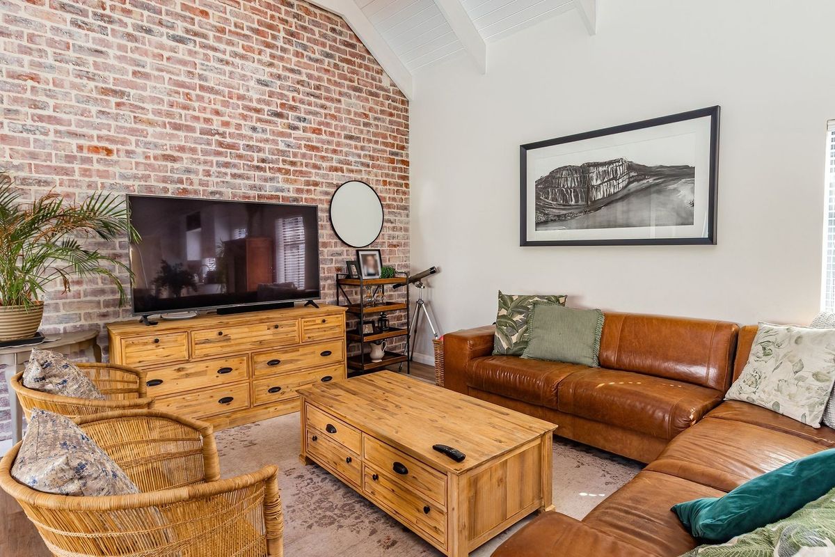 A cozy living room featuring a striking exposed brick feature wall, vaulted ceilings with exposed rafters, and durable laminate flooring.