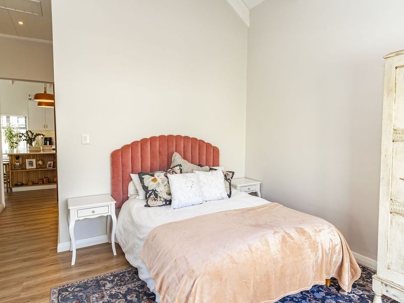 A bright bedroom featuring vaulted ceilings and laminate flooring, with a view through to the adjacent kitchen area.