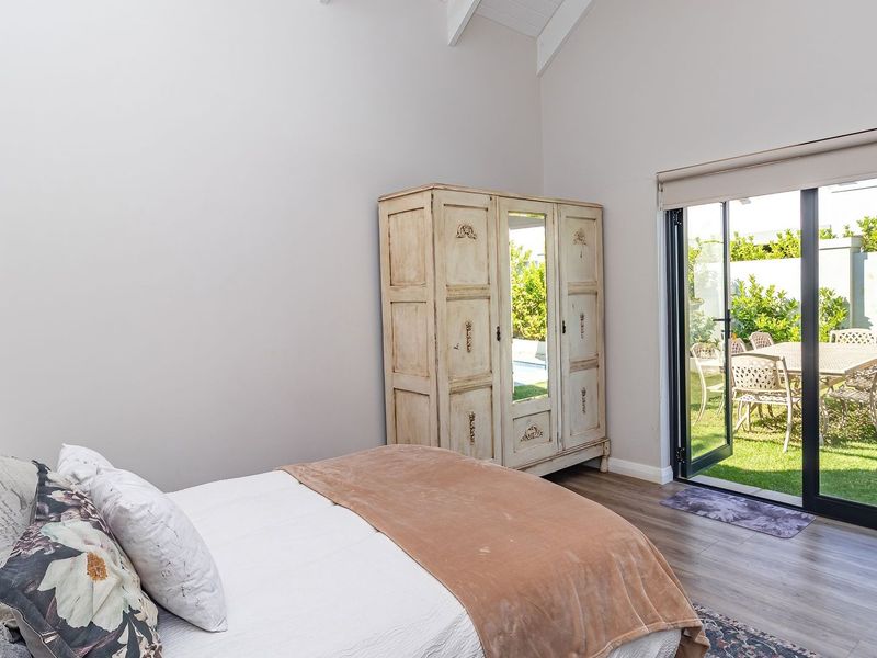 A bright bedroom featuring vaulted ceilings, laminate flooring, and sliding glass doors that provide direct access to the garden.