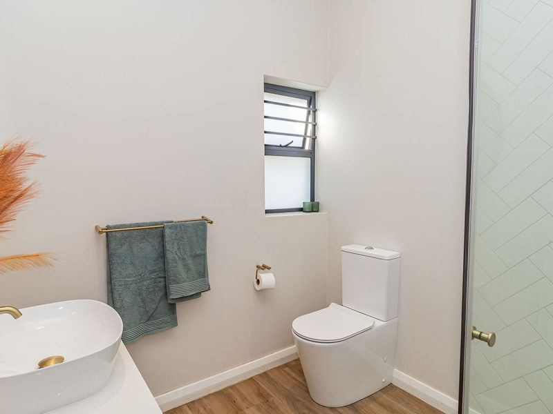 Modern bathroom featuring a vessel sink with brass fixtures, a glass-enclosed shower with herringbone tiling, and wood-look flooring.