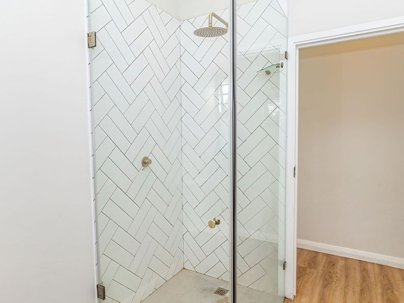 Modern bathroom shower featuring white herringbone wall tiles, a glass enclosure, and contemporary brass fixtures.