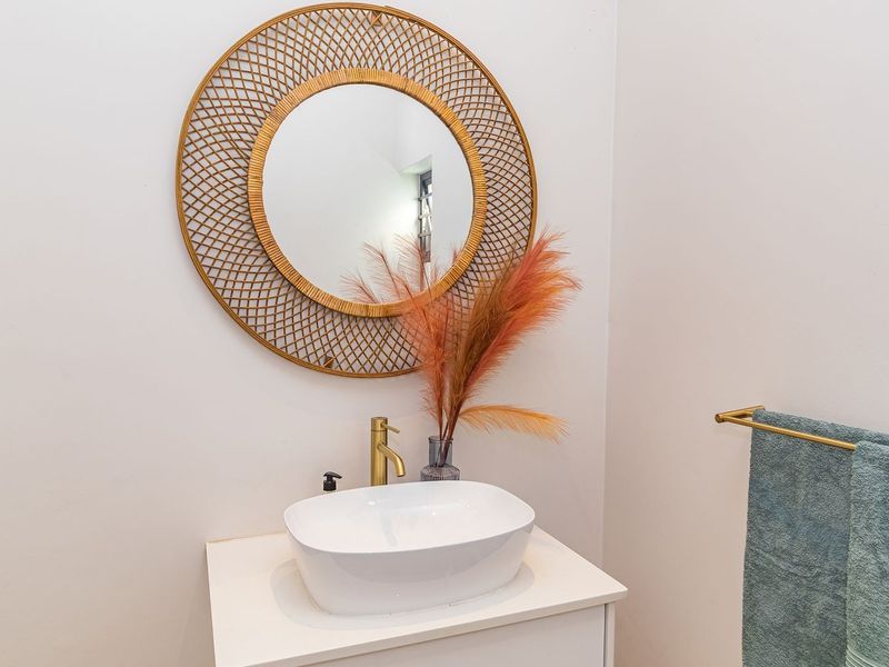 A modern bathroom vanity area featuring a white vessel sink, brass faucet, and a decorative circular wall mirror.