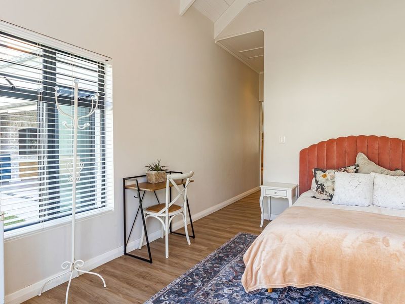 A bright bedroom featuring vaulted ceilings, laminate flooring, and large windows with fitted blinds, offering a clean and well-maintained living space.
