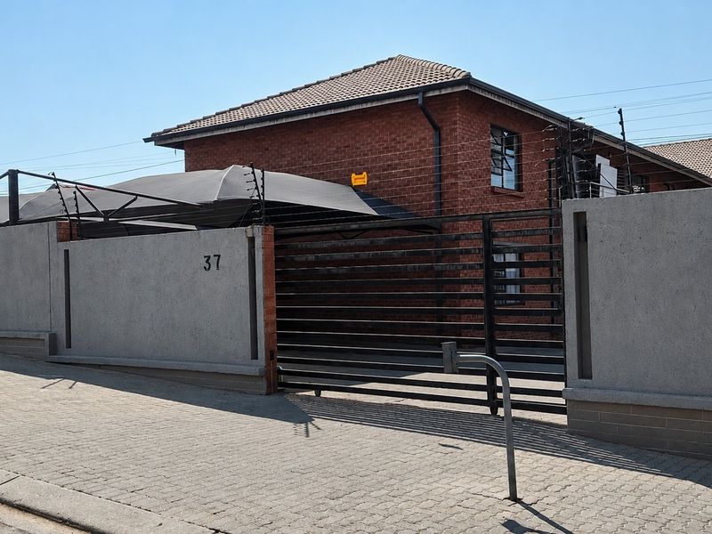 Front view of a brick house featuring a secure perimeter wall with electric fencing, a sliding gate, and a shade cloth carport.
