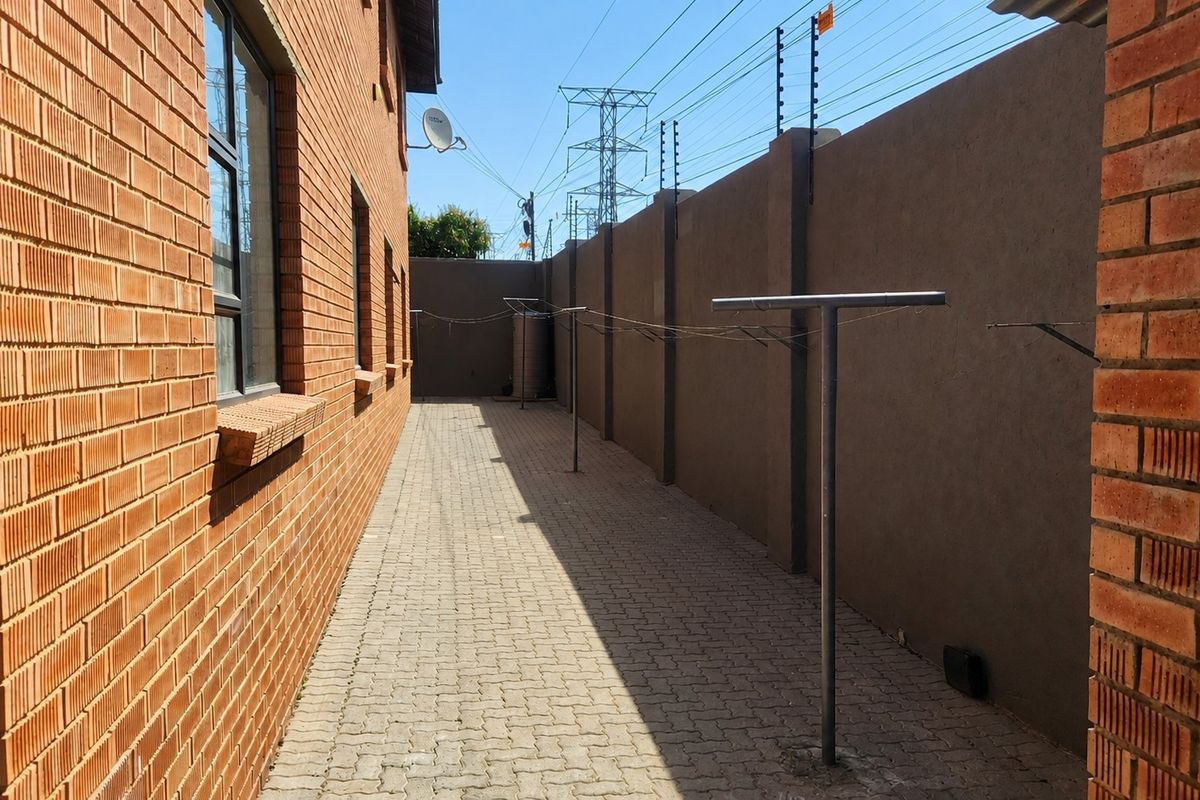 A side exterior walkway featuring brick wall construction, paved flooring, and a secure boundary wall with electric fencing.
