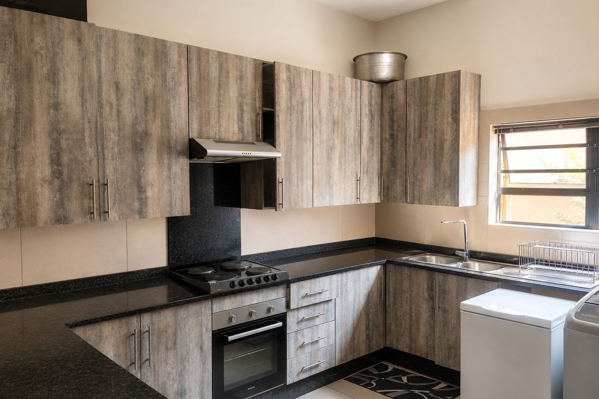 A functional kitchen featuring wood-look cabinetry, black granite countertops, built-in oven, hob, extractor fan, and a stainless steel double sink.