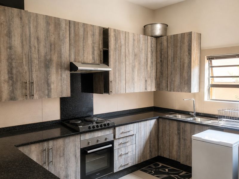 A functional kitchen featuring wood-look cabinetry, black granite countertops, built-in oven, hob, extractor fan, and a stainless steel double sink.
