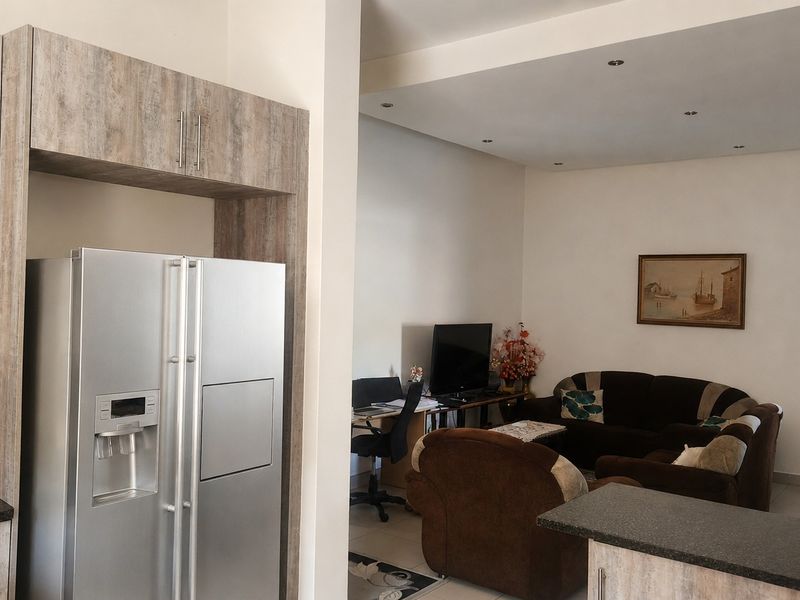 Open-plan living area featuring a modern kitchen with wood-look cabinetry, granite countertops, and tiled flooring, seamlessly flowing into the adjacent lounge space.